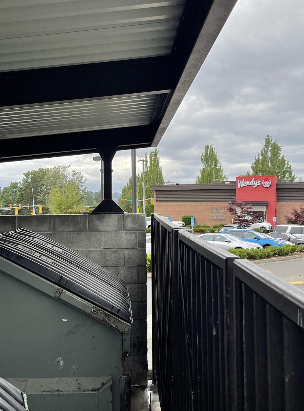The dumpster enclosure behind a Wendy's, photographed from behind the fence